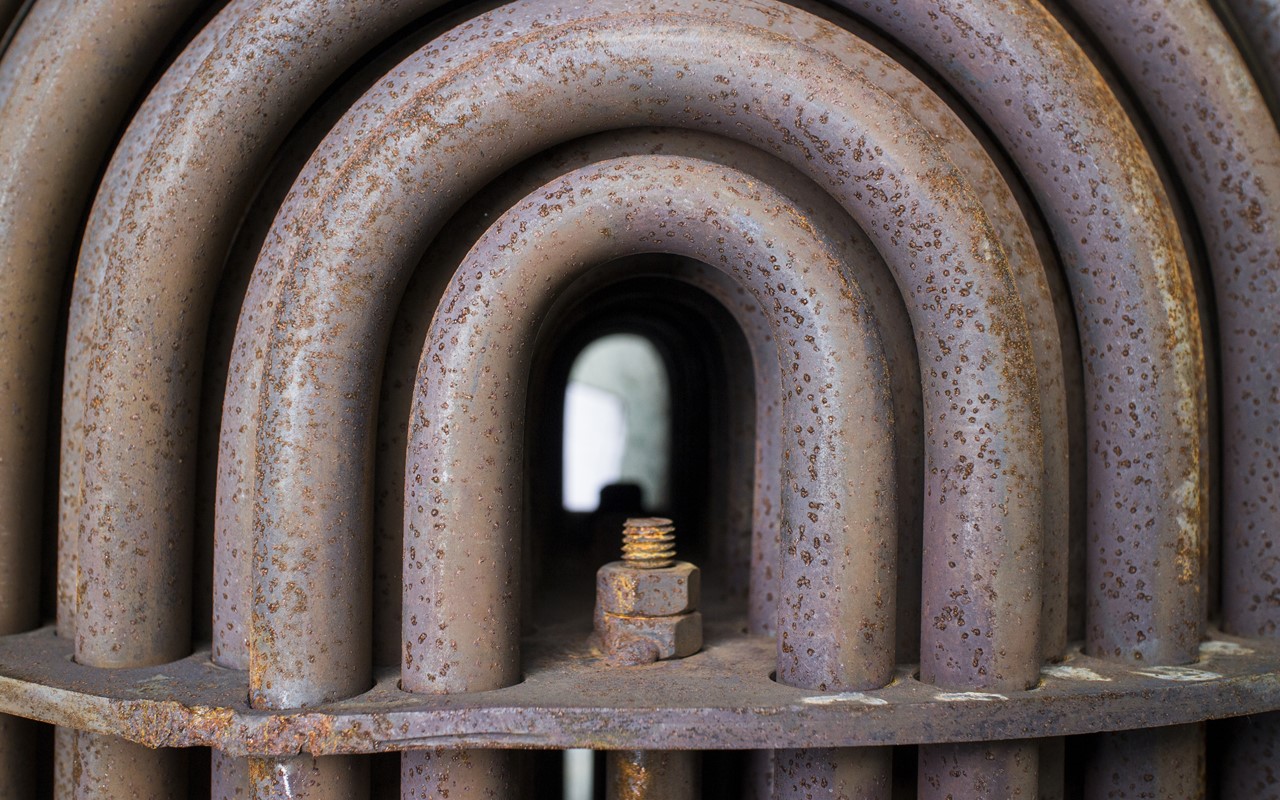 Close-up of a rusted heat exchanger tube bundle, concentric U-bends around a bolt at the centre