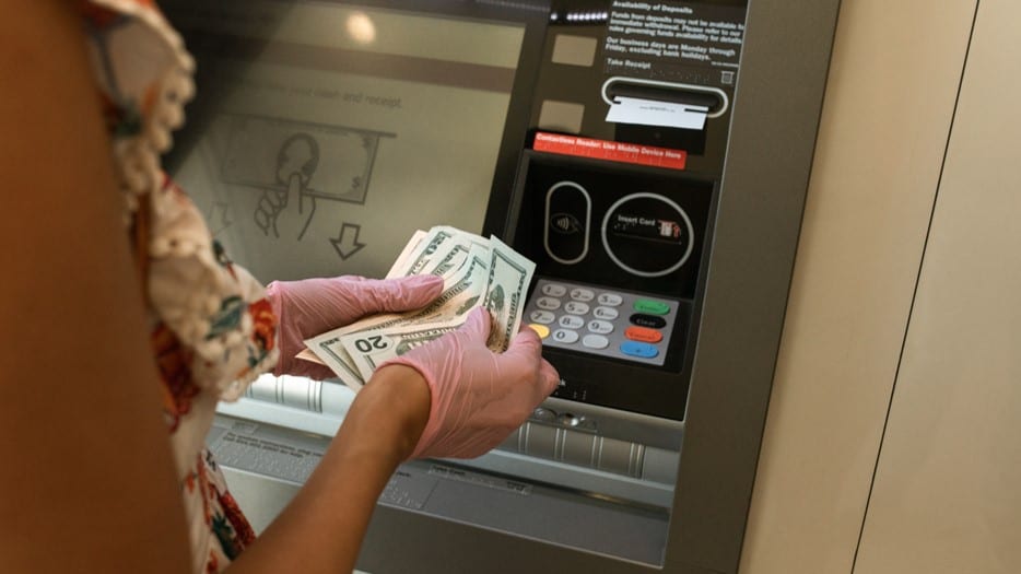 A person in pink disposable gloves counting banknotes at a cash machine
