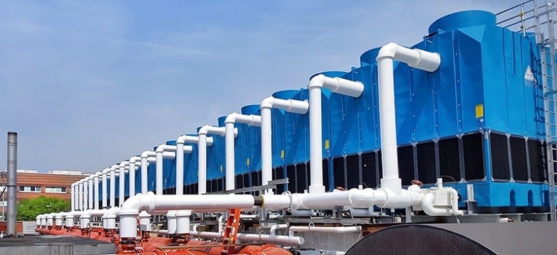 A long row of blue cooling towers on a roof, connected by white pipework
