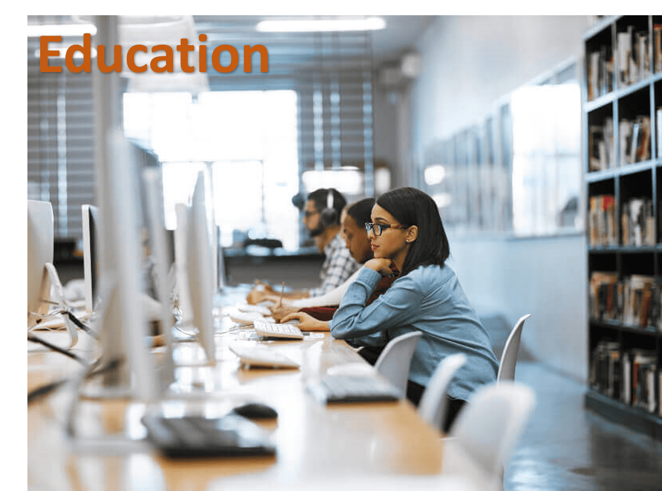 Students working at a row of desktop computers along a library bench, with the word "Education" across the top