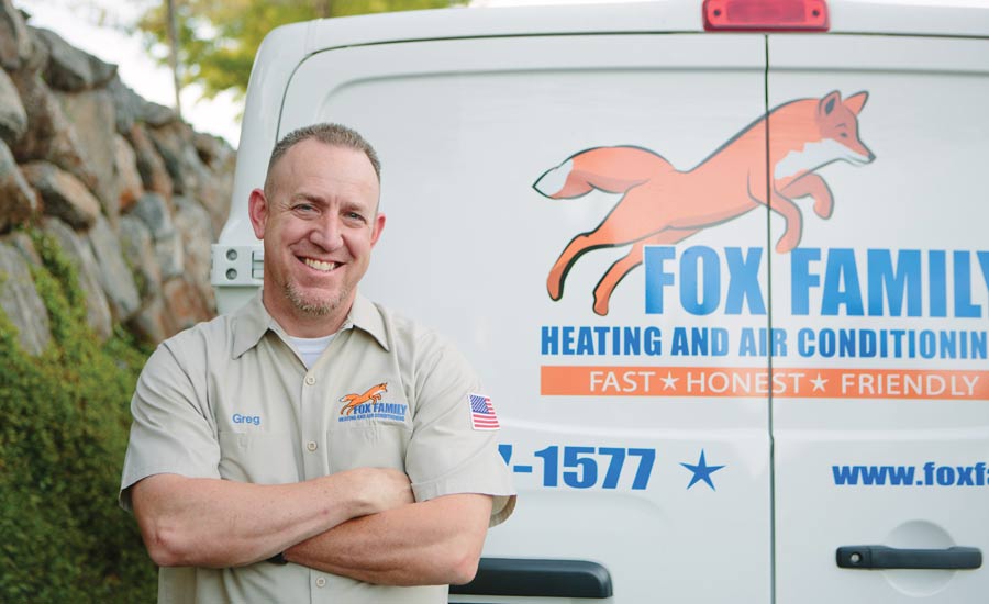 A man standing with his arms folded in front of a Fox Family Heating and Air Conditioning van, his work shirt embroidered "Greg"