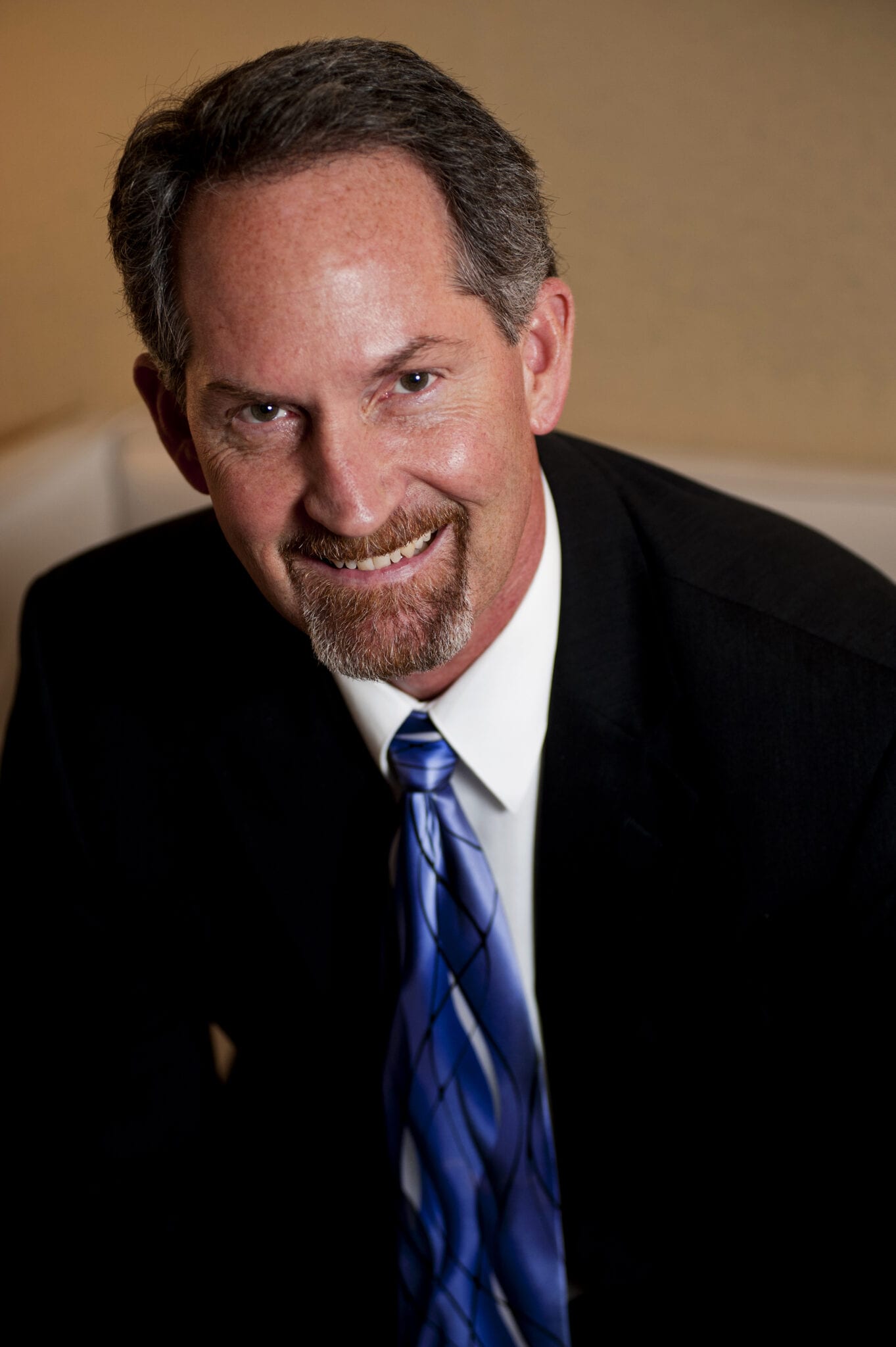 Portrait of a man in a dark suit and blue tie against a warm background