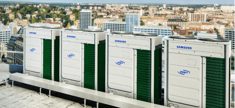 Four Samsung DVM S outdoor VRF units in a row on a rooftop, a city skyline behind