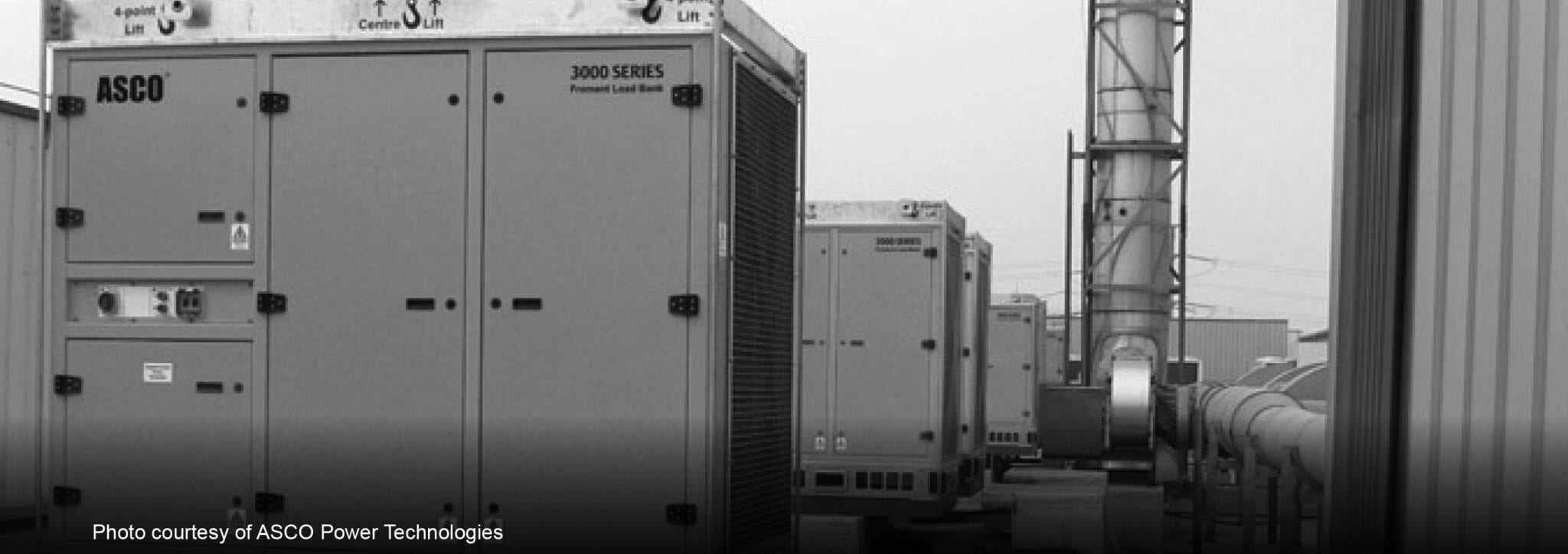 Black and white photograph of ASCO 3000 Series permanent load banks standing in a row outdoors beside ducting, captioned "Photo courtesy of ASCO Power Technologies"