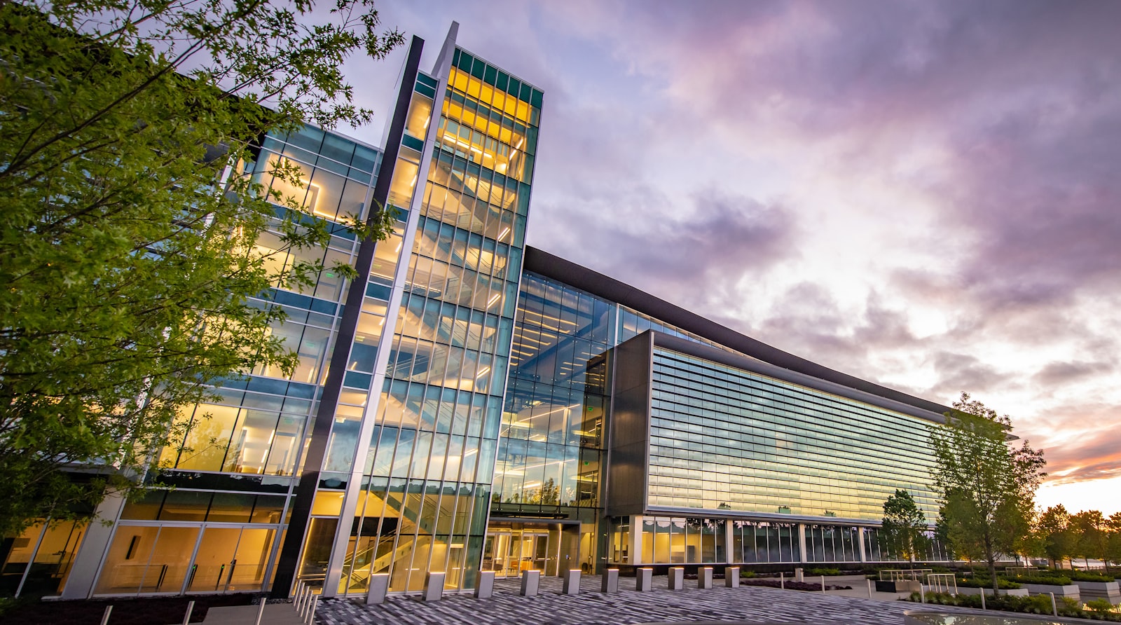 A modern glass-fronted corporate office building photographed at dusk, its interior floors lit from within