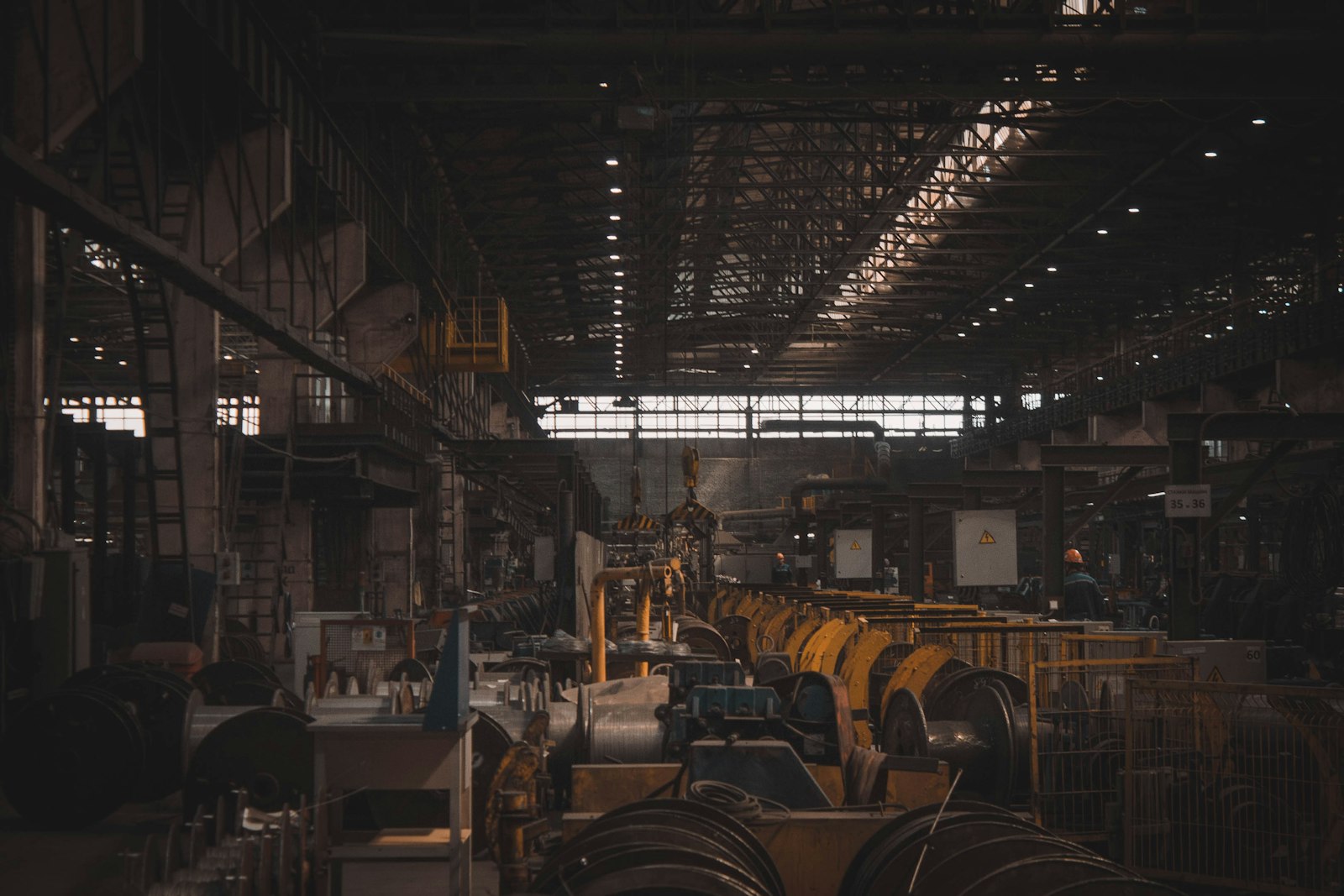 A large, dimly lit factory hall with overhead crane rails and rows of yellow production machinery running into the distance