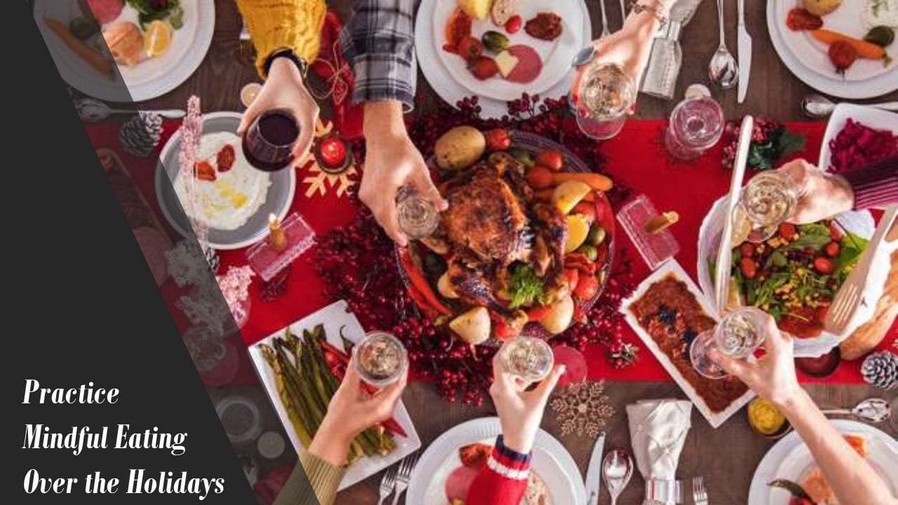A festive table shot from above, hands reaching in with glasses over a roast and side dishes, captioned "Practice Mindful Eating Over the Holidays"