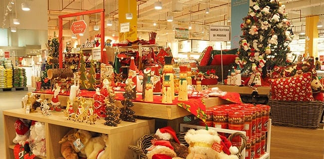 A department store Christmas display of decorations, soft toys and gift tins, with lit trees behind