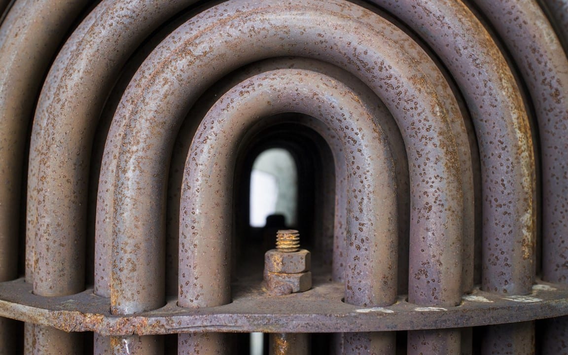 Close-up of a rusted heat exchanger tube bundle, concentric U-bends around a bolt at the centre