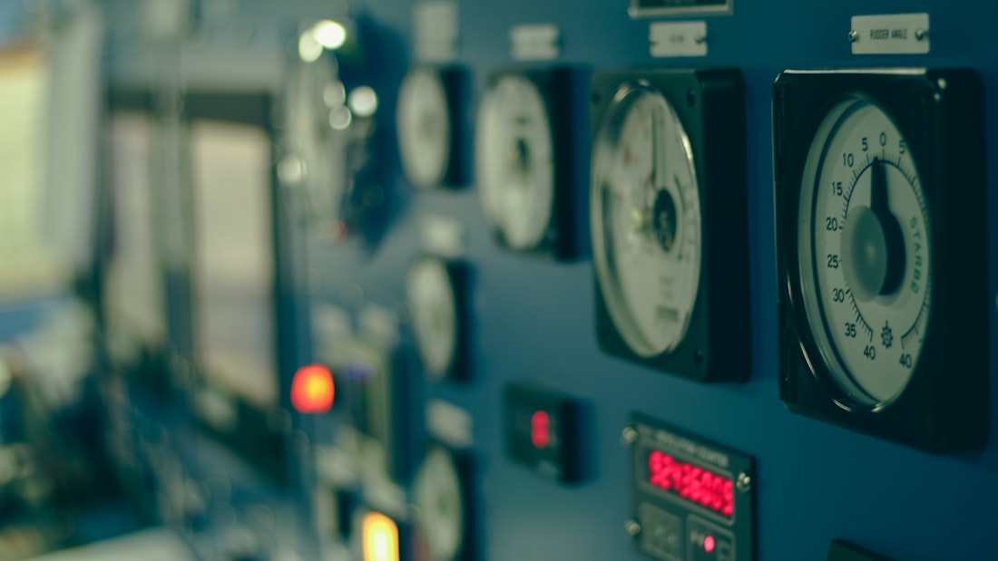 A control-room panel of analogue gauges and lit indicator lamps, angled away into shallow focus