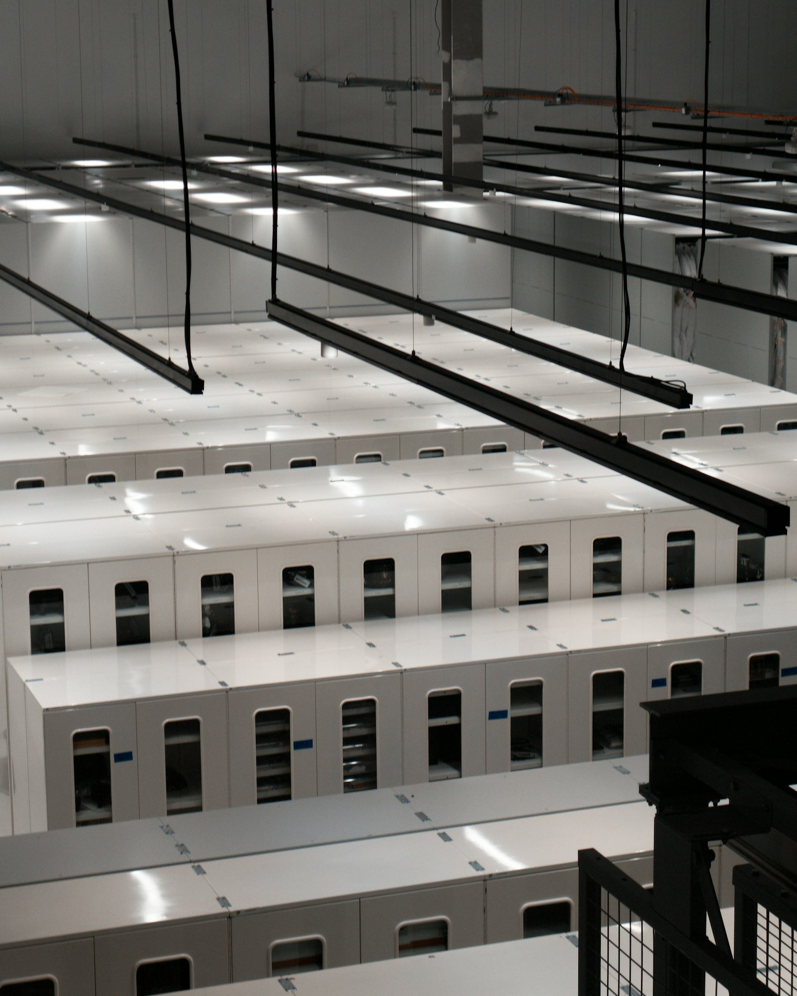 An empty data hall of white enclosed server cabinets in long rows, with cable trays hanging from the ceiling above them