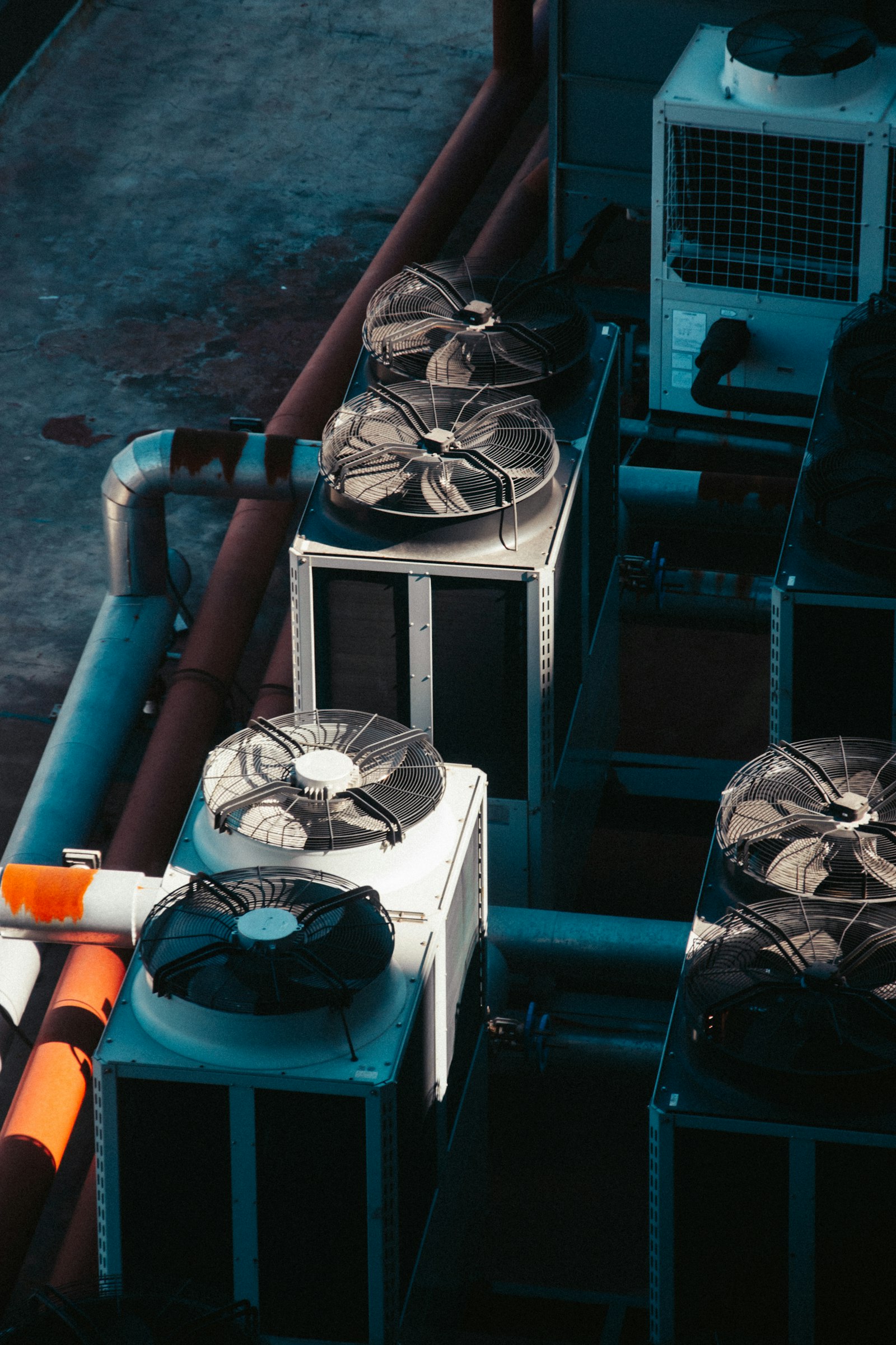 Looking down on a row of rooftop condenser units, their large fans facing up, with insulated refrigerant piping running between them
