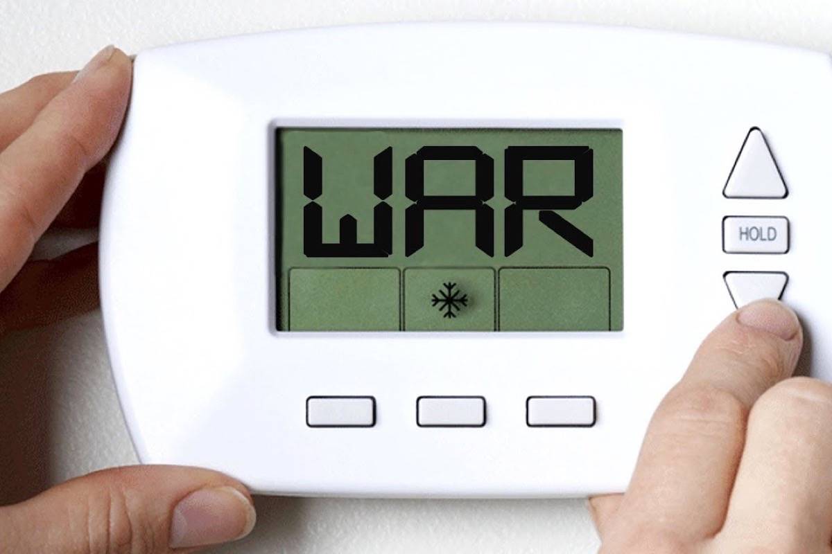 Two hands on a wall thermostat, one pressing the down arrow, the display reading "WAR" above a snowflake icon
