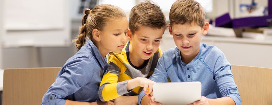 Three children leaning together over a tablet at a school desk